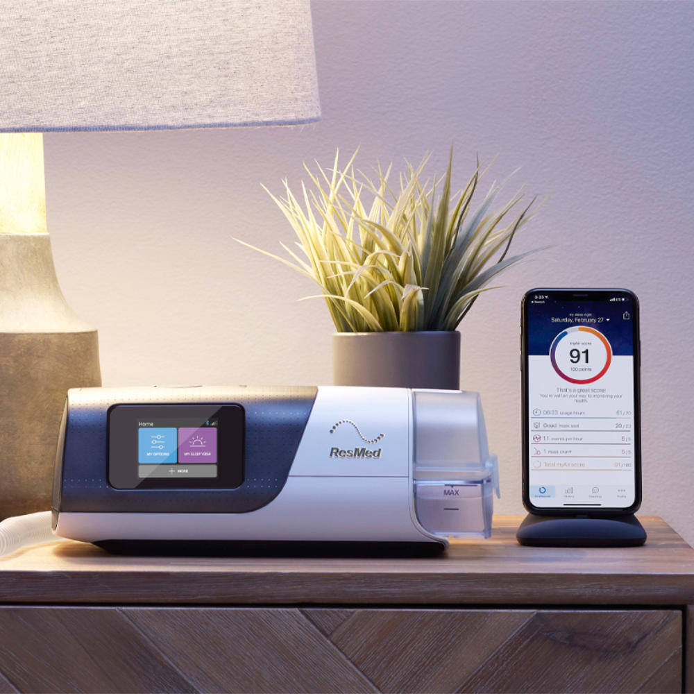 Resmed AirSense 11 CPAP Machine with myAir app on nightstand with a plant and lamp.