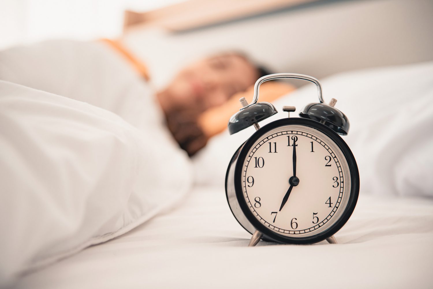 Vintage alarm clock on a white bed with a person partially visible in the background