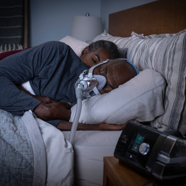 AirSense 10 CPAP machine on nightstand with person sleeping beside it with a full face mask on