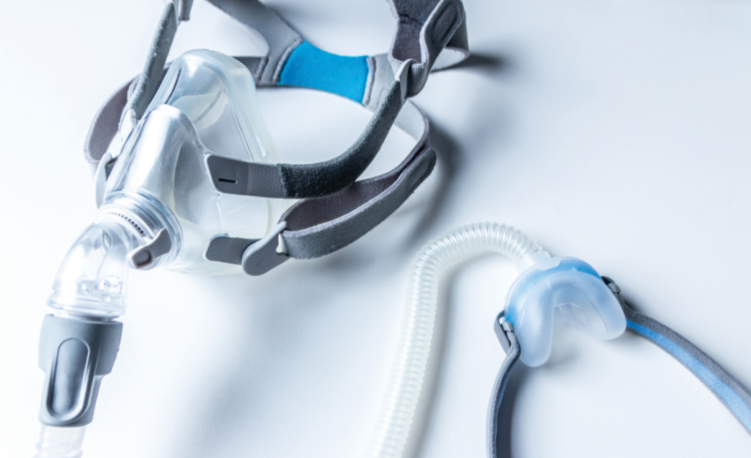 A full face CPAP mask with tubing alongside a nasal CPAP mask with a short hose on a light gray background.