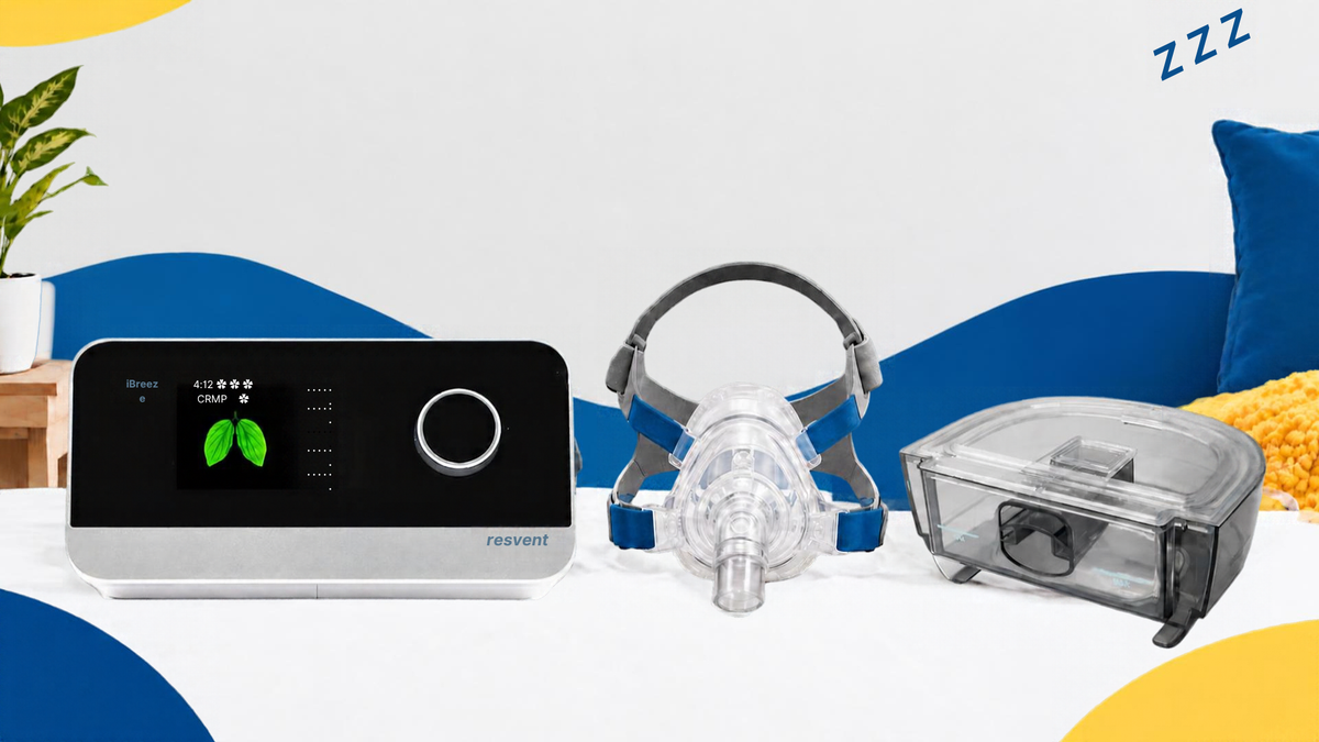 An ibreeze CPAP machine a full face mask and water tank set displayed on a white surface with a stylized studio background. The set includes blue and yellow decor with a plant in the background