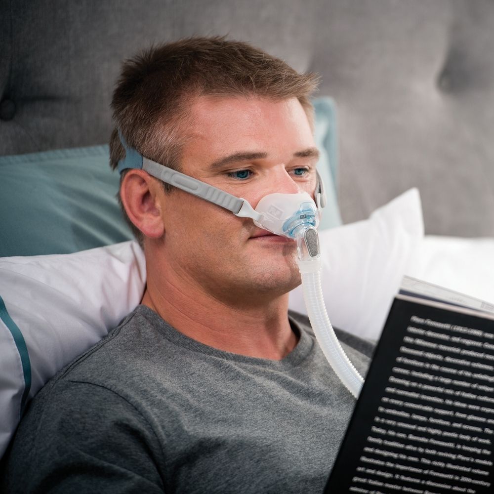 Person wearing the F&P Brevida Nasal Pillow Mask while reading a book in bed