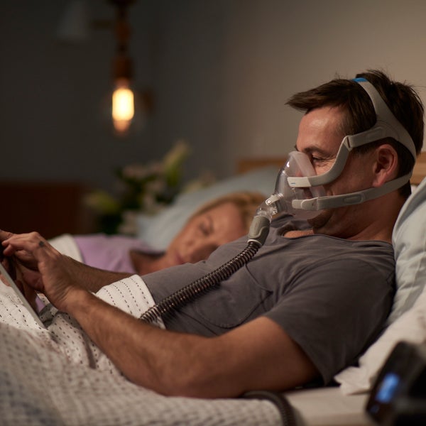 Man using the ResMed AirFit F20 full face CPAP mask while in bed using a tablet