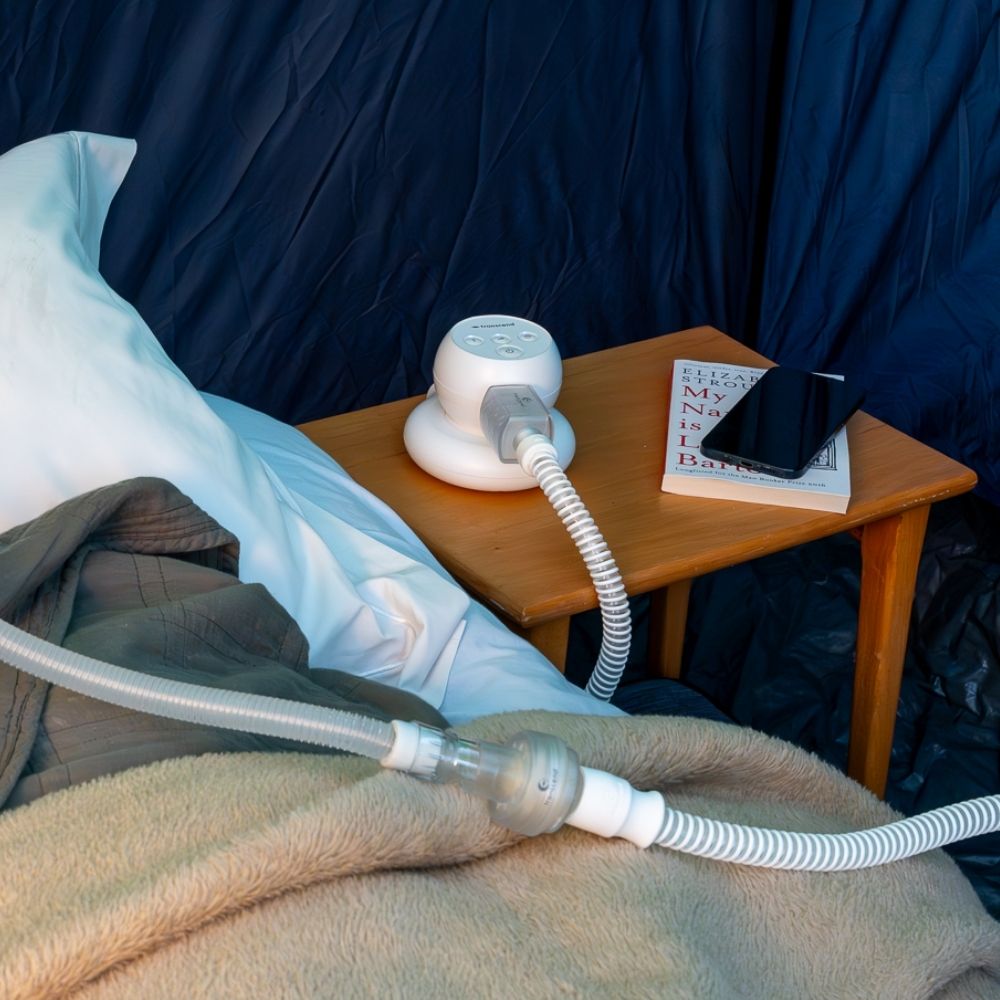 Transcend Micro CPAP device in use and connected to a tube and HME inside a tent