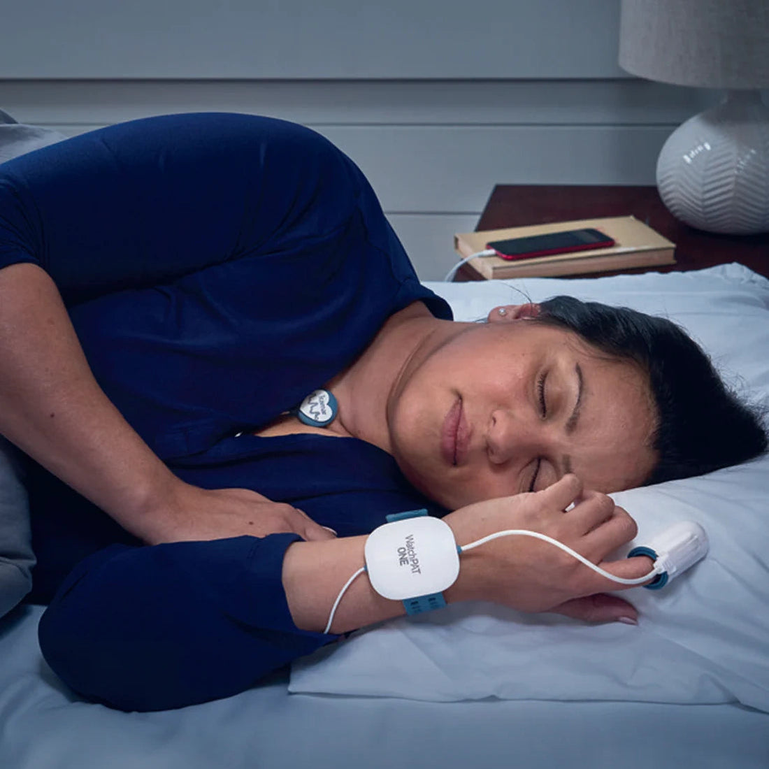 Person lying comfortably in bed at home with the WatchPAT ONE home sleep apnea testing device worn on the wrist, finger and sensor on the chest
